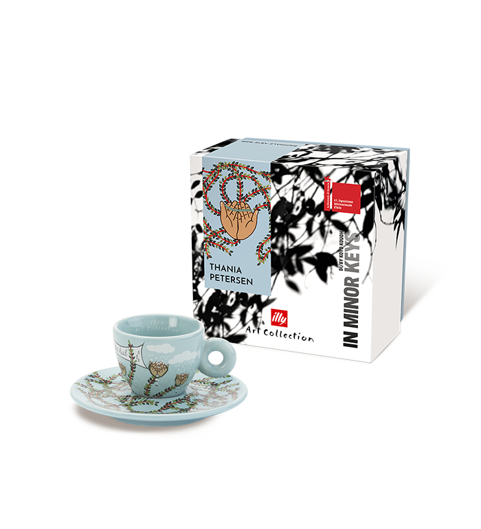 A light blue ceramic espresso cup and saucer with botanical illustrations, displayed in front of its white and black packaging box. The box features the text 'THANIA PETERSEN', 'IN MINOR KEY', and the 'il Mio Caffe Art Collection' logo.