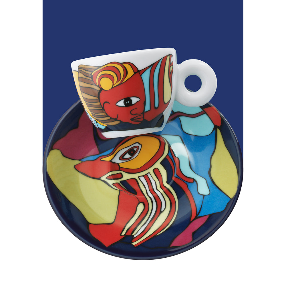 A white ceramic espresso cup and matching saucer set, both decorated with a colorful abstract face illustration in red, yellow, blue, and cream, set against a dark blue background.